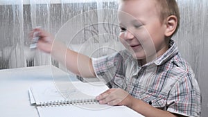 Little caucasian boy draws doodles and scribbles furiously in notebook at table