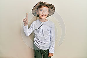 Little caucasian boy kid wearing explorer hat smiling with an idea or question pointing finger up with happy face, number one