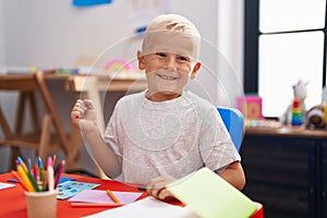 Little caucasian boy painting at the school screaming proud, celebrating victory and success very excited with raised arm