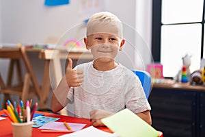 Little caucasian boy painting at the school smiling happy and positive, thumb up doing excellent and approval sign