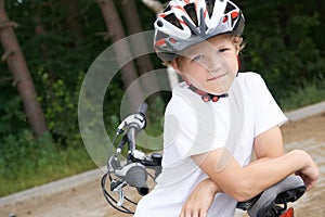 Little Caucasian boy in protective helmet stands leaning on the bike posing for the camera. Teenager ready to ride