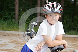 Little Caucasian boy in protective helmet stands leaning on the bike posing for the camera. Teenager ready to ride