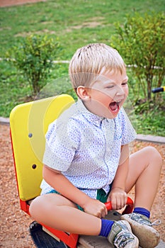 Little caucasian boy screaming on a swing balancer on the kid playground.