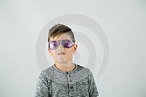 Little caucasian boy standing in a studio setting on a white backdrop with rock star purple sunglasses and attitude.
