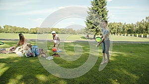 Little caucasian boy throws a ball, girl catches, picnic, family background