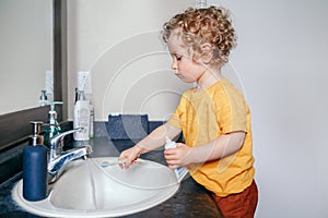 Little Caucasian boy toddler brushing teeth in bathroom at home. Health hygiene and morning routine for children. Cute funny child