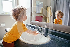 Little Caucasian boy toddler washing hands in bathroom at home. Health hygiene and morning routine for children. Cute funny child