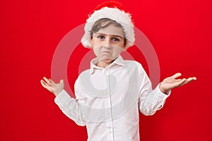 Little caucasian boy wearing christmas hat over red background shouting and screaming loud to side with hand on mouth