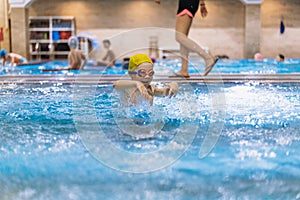 little caucasian boy wearing goggles splashing in small pool in sport centre