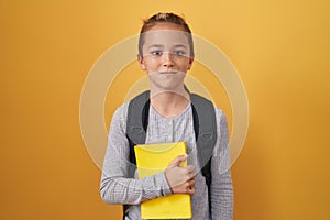 Little caucasian boy wearing student backpack and holding book thinking attitude and sober expression looking self confident