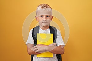 Little caucasian boy wearing student backpack and holding book thinking attitude and sober expression looking self confident