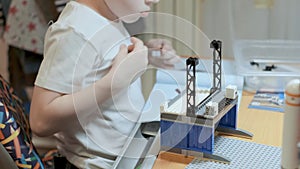 Little caucasian boy in white t-shirt sitting at table playing with constructor