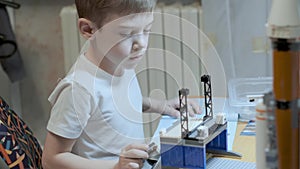 Little caucasian boy in white t-shirt sitting at table playing with constructor