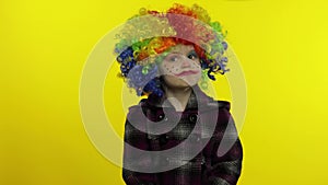 Little caucasian child girl clown in rainbow wig making silly faces, hakes her head. Halloween