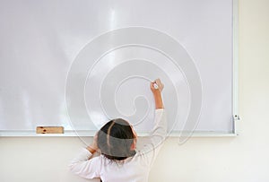 Little caucasian child girl writing something on whiteboard with a marker in the classroom. White board with copy space for text.