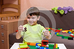 Little caucasian child playing with lots of colorful plastic blocks indoor. Kid boy wearing shirt and having fun building creating