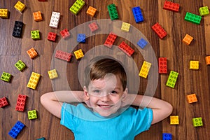 Little caucasian child playing with lots of colorful plastic blocks indoor. Kid boy wearing shirt and having fun building creating