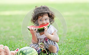 Little Caucasian cute girl holding sliced watermelon and enjoy eating or biting while picnic at park. Happy healthy child sitting