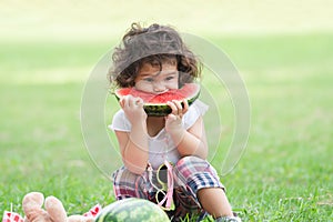 Little Caucasian cute girl holding sliced watermelon and enjoy eating or biting while picnic at park. Happy healthy child sitting