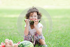 Little Caucasian cute girl holding sliced watermelon and enjoy eating or biting while picnic at park. Happy healthy child sitting