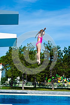 Little caucasian female 8 years old girl jumping from a diving platform