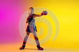 Little caucasian female kick boxer training on gradient background in neon light, active and expressive
