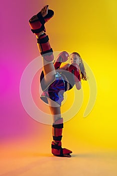 Little caucasian female kick boxer training on gradient background in neon light, active and expressive