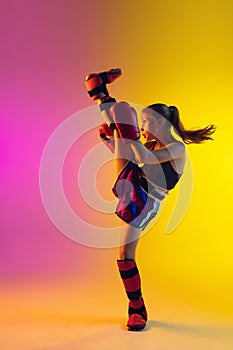 Little caucasian female kick boxer training on gradient background in neon light, active and expressive