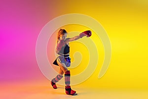 Little caucasian female kick boxer training on gradient background in neon light, active and expressive