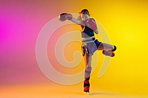 Little caucasian female kick boxer training on gradient background in neon light, active and expressive