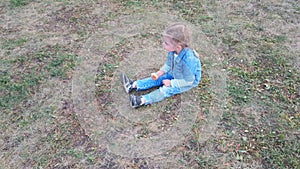 Little Caucasian girl with blond hair in a denim suit playing in the Park.