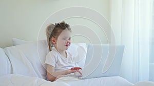Little caucasian girl checks a laptop in bed. Modern Kids and Gadgets. The girl scrolls social networks. Electronic