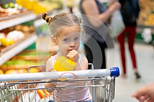 Little Caucasian girl chooses fresh vegetables in the supermarket
