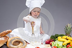 Little Caucasian Girl In Cook Uniform Making a Mix of Flour, Eggs and Vegetables With Whisk In Studio