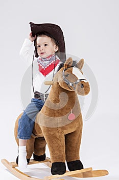 Little Caucasian Girl in Cowgirl Clothing Posing On Symbolic Horse Against White