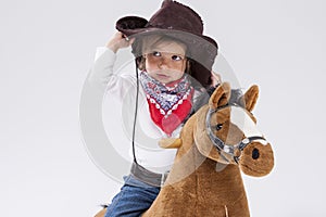 Little Caucasian Girl in Cowgirl Clothing Posing On Symbolic Horse Against White. Holding Her Stetson