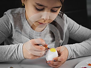 Little caucasian girl in a gray turtleneck enthusiastically paints an Easter egg