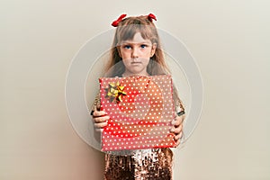 Little caucasian girl kid holding red gift relaxed with serious expression on face