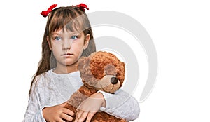 Little caucasian girl kid hugging teddy bear stuffed animal thinking attitude and sober expression looking self confident