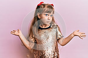 Little caucasian girl kid wearing festive sequins dress clueless and confused expression with arms and hands raised