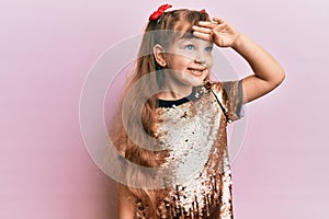 Little caucasian girl kid wearing festive sequins dress very happy and smiling looking far away with hand over head