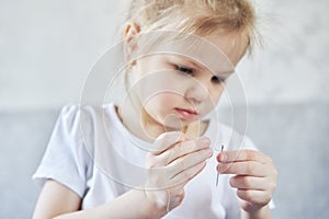 Little Caucasian girl learns to insert a thread into a needle.