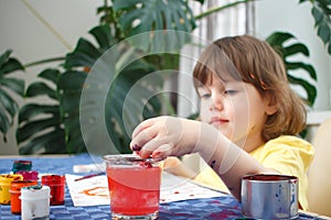 Little caucasian girl paints small toy figures in home interior. A cute three year old child is engaged in creativity