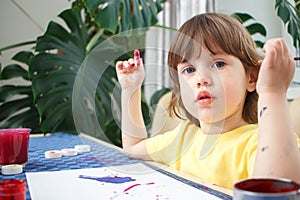 Little caucasian girl paints small toy figures in home interior. A cute three year old child is engaged in creativity