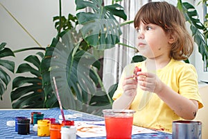 Little caucasian girl paints small toy figures in home interior. A cute three year old child is engaged in creativity