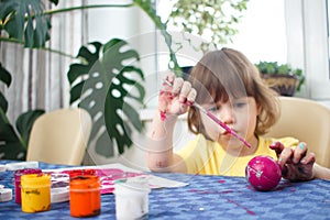 Little caucasian girl paints small toy figures in home interior. A cute three year old child is engaged in creativity