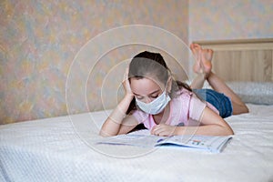 Little caucasian girl in a protective mask writes in a notebook during quarantine. Distance learning online education