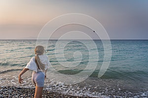 Little Caucasian girl running on the beach to the blue sky with sunset