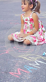 Little Caucasian girl sits on the asphalt surrounded by chalk drawings