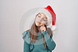 Little caucasian girl wearing christmas hat thinking concentrated about doubt with finger on chin and looking up wondering